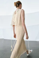 Vestido midi de viscosa con efecto arrugado, cuello redondo y diseño sin mangas. Presenta una sobrecapa superior con bordados detallados y entredoses, con cordones laterales ajustables terminados en borlas.
