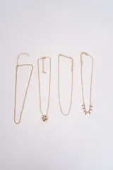 Set de cuatro collares de cadena fina en color dorado. Incluye una cadena simple, una con dije de corazón, una con detalles de perlas pequeñas y una con dijes colgantes en forma de cruz.