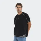 Remera negra de corte boxy con costuras a la vista en color blanco. Presenta un pequeño logo estampado en el centro del pecho y una frase bordada en la parte inferior. Cuenta con mangas raglán.
