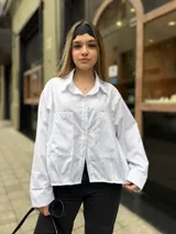 Camisa blanca de diseño oversize, con mangas largas, bolsillos frontales con solapa y cierre de botones.