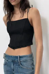 Top crop corsetero negro de popelín con escote recto, tirantes finos ajustables con lazada y bajo acabado con volante. Tiene forro interior a tono y cierre de cremallera en la espalda.