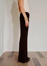 Pantalón flare de tiro medio, color marrón oscuro, con aberturas laterales en el bajo, bolsillos laterales y bolsillos de ribete en la parte posterior. Cierre oculto con botón, gancho y cremallera, e incluye forro interior.