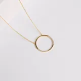 Collar de cadena fina con dije circular, elaborado en plata 925 con baño de oro. El dije presenta un diseño minimalista con incrustaciones de circonias en dos secciones opuestas del círculo.
