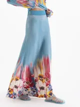 Pollera larga de tiro alto con calce evasé, confeccionada en tejido celeste con cintura elastizada lisa y estampado floral multicolor en el ruedo.
