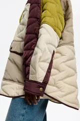 Abrigo acolchado de corte recto con diseño patchwork en tonos burdeos, beige y verde oliva. Presenta cuello camisero de pana, cierre frontal con botones de presión, bolsillos de tapeta en el bajo y bolsillos de vivo en el pecho.