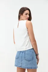 Blusa de denim blanco sin mangas, con cuello redondo y volados a lo largo de las costuras laterales.