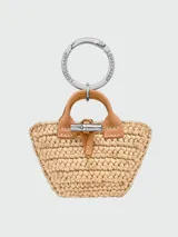 Llavero Longchamp modelo Roseau Raffia con diseño en miniatura de bolso tipo canasto de rafia con asas y detalles en cuero marrón y herrajes metálicos plateados con cierre de botón de bambú.