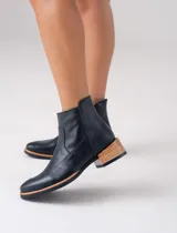 Bota corta de cuero vacuno color negro, con diseño de punta fina y cierre lateral. Presenta un taco bajo de madera y una entresuela de goma en tono natural que contrasta con el cuerpo de la bota.