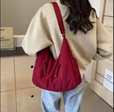 Bolso hobo grande color gris topo, de tela suave y liviana, con correa de hombro ajustable y dos bolsillos frontales con cierre.