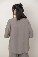 Blusa de lino color marrón oscuro, con escote redondo, mangas cortas amplias y detalle de alforzas verticales en el lateral derecho.