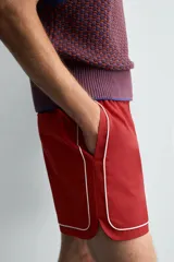 Short de algodón color rojo oscuro, de corte regular fit, con cintura ajustable mediante cordón blanco. Presenta ribetes o vivos de contraste en color blanco bordeando los laterales, el bajo y los bolsillos.