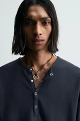 Camiseta de manga larga para hombre con corte relajado, confeccionada en tejido con estructura waffle. Presenta un cuello redondo tipo panadero con cierre frontal de botones a presión.