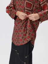 Camisa de seda con cuello camisero, manga larga y bolsillo frontal. Presenta un diseño estampado geométrico de cuadrados en tonos marrones y azul oscuro.