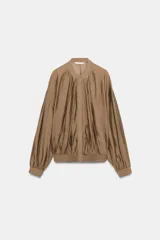 Camisa fluida de Zara Woman Collection, confeccionada en hilatura con mezcla de viscosa en tono tostado. Presenta cuello redondo, mangas largas con puños elásticos y diseño fruncido en la parte delantera. Dispone de cierre frontal con botones ocultos por solapa.