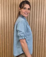 Camisa de denim de algodón celeste, con cierre frontal de botones, cuello alto con volados y mangas cortas abullonadas con puños elastizados fruncidos.