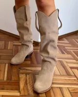Bota estilo tejana de caña alta, confeccionada en gamuza, con taco cuadrado y diseño de costuras decorativas.