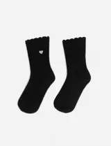 Par de medias negras de tejido acanalado, caña media, con borde superior festoneado y un pequeño corazón bordado en color plateado en la parte superior de una de las medias.