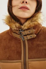 Campera estilo aviador en tonos tostados, con diseño acolchado y paneles de gamuza en la parte superior. Presenta cuello alto con doble hebilla, cierre frontal completo y detalles de corderito sintético en el cuello y el ruedo.
