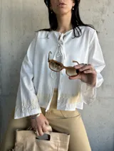 Chaqueta blanca de algodón con bordados florales en puños y ruedo, escote con lazos y mangas largas acampanadas.