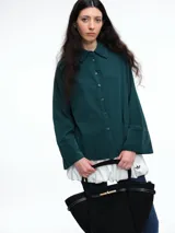 Camisa oversize de lyocell color verde oscuro, con cuello clásico, cierre frontal de botones y mangas largas con puños anchos. Presenta un corte relajado y fluido.