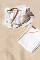 Bolso de playa o calle de lino blanco con bordados estilo broderie anglaise. Presenta volados superpuestos con terminación desflecada y forro interno de gabardina de algodón. Incluye correa desmontable de cuero color camel.