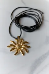 Collar con dije de acero quirúrgico en forma de flor tipo margarita, montado sobre un tiento de cuero negro.