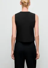 Chaleco de sastrería negro con cuello redondo, sin mangas, diseño recto y bolsillos de ribete laterales. Cuenta con cierre frontal de botones con efecto joya.