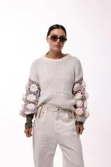 Sweater de punto con cuerpo liso en color negro y mangas largas tejidas en crochet gris con aplicaciones de flores en relieve color blanco.
