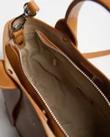 Cartera tipo tote de cuero sintético color habano, con doble asa de mano, tiras frontales decorativas y correa regulable y extraíble. Cuenta con el logo de la marca impreso en plateado en el frente.