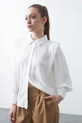 Camisa negra de estilo sastrero con cuello clásico, frente abotonado y mangas largas con puños ajustados. Presenta un diseño con hombreras sutiles que aportan estructura a la prenda.
