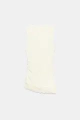 Camiseta ajustada (slim fit) color crema, con cuello redondo y mangas sisa. Presenta frunces laterales y un bajo asimétrico con detalle de encaje a tono.