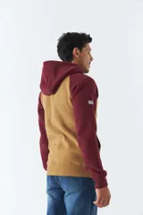 Buzo canguro gris con mangas ranglan azul marino, capucha con cordones ajustables y bolsillo delantero. Estampado frontal con el logo de la marca y el año de fundación.