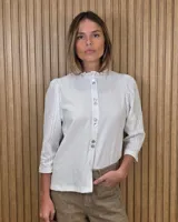 Camisa de algodón color blanco, con cuello alto con volados, mangas tres cuartos con detalles de bordado ingles y cierre frontal con botones de nácar.
