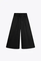 Pantalón negro de tiro medio, estilo culotte, con cintura elástica fruncida y piernas muy anchas. Posee bolsillos laterales ocultos.