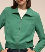 Campera bomber femenina color beige claro, confeccionada en tejido Airflow texturado. Presenta cuello solapa, cierre frontal de cremallera y puños y bajo elásticos.