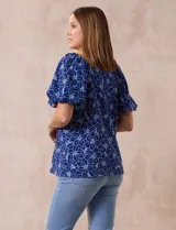 Blusa azul con estampado floral blanco, cuello cuadrado, mangas cortas abullonadas y frunce en los hombros.