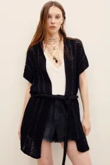 Chaleco largo de punto negro con diseño abierto y cinturón ajustable en la misma tela. Presenta detalles de hilos metalizados y tramas caladas.