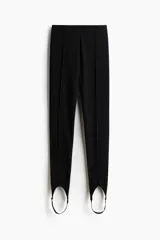 Leggings negros de tiro alto en punto elástico, con pliegues frontales pespunteados y estribos en los tobillos.