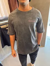 Remera de corte oversize con efecto de lavado ácido en color gris oscuro. Presenta un estampado gráfico en color rosa en la parte posterior con el texto 'BOHEMIAN DSG'.