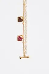 Collar doble de estilo delicado, compuesto por una cadena de perlas irregulares y una cadena dorada con pequeños dijes colgantes en forma de corazón esmaltados en tonos marrón oscuro, vino, verde menta y rosa pálido. La cadena dorada también presenta pequeñas cuentas metálicas. El cierre es tipo 'toggle' (anillo y barra) en tono dorado.