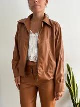 Campera marrón de cuero sintético con cierre frontal, cuello camisero y costuras decorativas en hilo blanco.