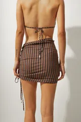 Falda corta tipo pareo con diseño de rayas verticales en tonos azul y negro. Presenta un lateral fruncido con cordón ajustable que permite regular el largo y el ajuste de la prenda.