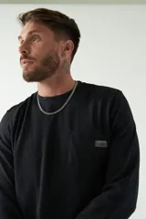 Remera de hombre negra de manga larga con puños, escote redondo y bolsillo en el pecho con etiqueta de marca.