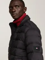 Campera acolchada negra de nailon con aislamiento térmico y acabado repelente al agua. Tiene cuello alto, cierre de cremallera, dos bolsillos delanteros y parche engomado del logo de Tommy Hilfiger en la manga.