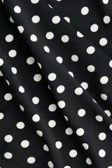Pollera midi negra con estampado de lunares blancos, tiro alto, cintura elástica con fruncidos laterales y abertura pronunciada en un lateral.