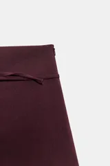 Falda pantalón de tiro medio en color bordó, con diseño cruzado en el frente y detalle de cinturón fino integrado con hebilla metálica.