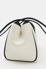 Bolso de hombro de diseño alargado en color blanco con detalles de bordes y asas largas en color negro. Cuenta con cierre imantado y bolsillo interior con cremallera.