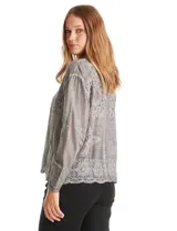 Camisa de algodón color gris con bordados florales en el frente y las mangas. Tiene cuello con solapa y cierre frontal con botones.