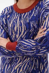 Sweater de punto con estampado animal print en tonos marrones, negros y blancos. Tiene cuello redondo, puños y bajo acanalados en color marrón y gris.