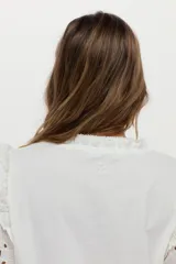 Blusa blanca con mangas abullonadas de broderie, cuello elevado con volados y detalles de volados en los hombros.